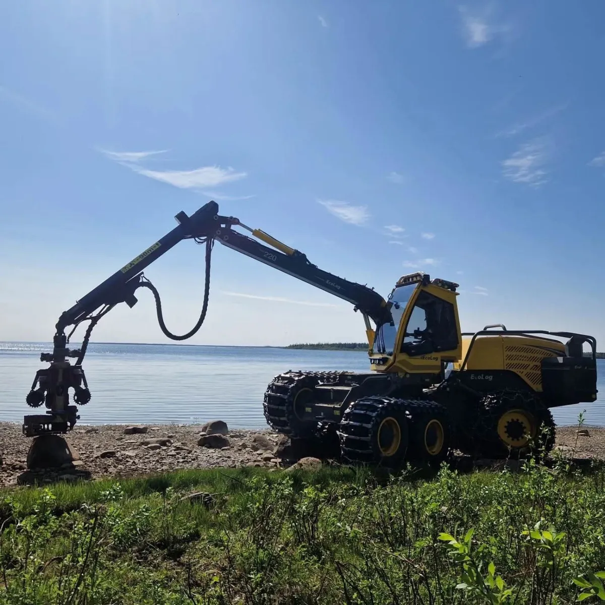 Gul skördare med utsträckt kran på en strand i Kalix, med havet och blå himmel bakom