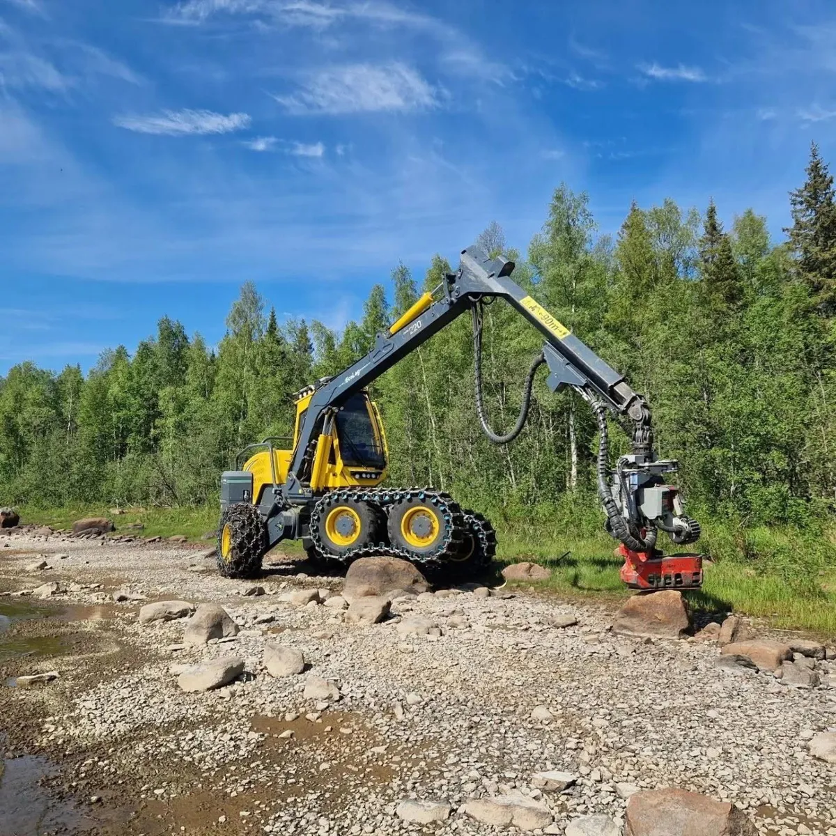 Gul skördare på en stenig strand framför grön lövskog